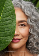 Close-Up of Smiling Mature Woman with Gray Curly Hair and Green Leaf