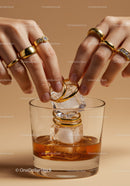 Hands Adorning Ice Cubes with Gold Rings over Whiskey Glass