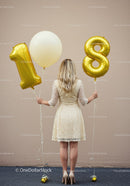 Woman holding golden 18th birthday balloons outdoors