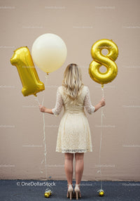 Woman holding golden 18th birthday balloons outdoors