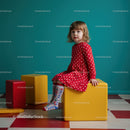 Little girl in red polka dot dress sitting on yellow block