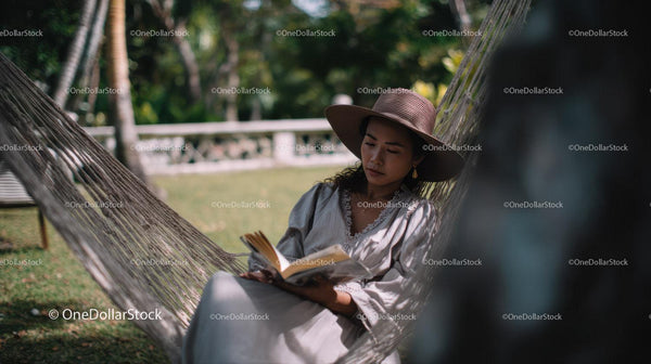 Woman Relaxing on Hammock in Tropical Garden Reading Book
