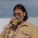 Young Woman Drinking Green Juice Wearing Sunglasses Outdoors