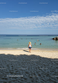 Woman in Straw Hat Walking on Sandy Beach with Ocean View