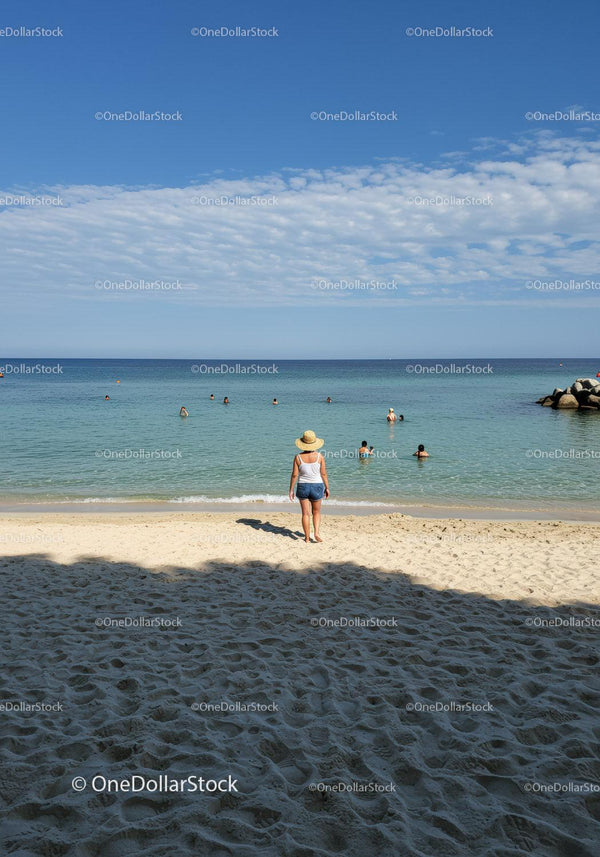 Woman in Straw Hat Walking on Sandy Beach with Ocean View