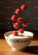 Fresh raspberries falling into creamy yogurt bowl