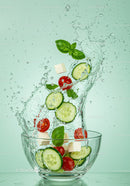 Fresh cucumber and tomato salad splashing into glass bowl
