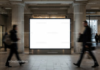 Busy commuters walking past large blank billboard indoors
