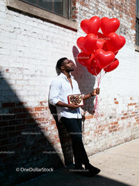 Man holding heart balloons and chocolates outdoors