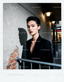 Confident woman in black blazer standing by urban wall