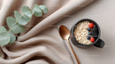 Black Ceramic Mug Filled with Oatmeal and Fresh Berries on Beige Silk