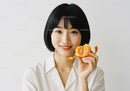 Smiling Woman Holding Fresh Orange Fruit in Bright Indoor Setting