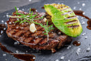 Grilled Steak with Avocado Slice and Garlic Garnish on Slate Plate