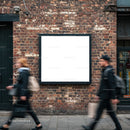 Two blurred pedestrians walking past blank billboard on brick wall
