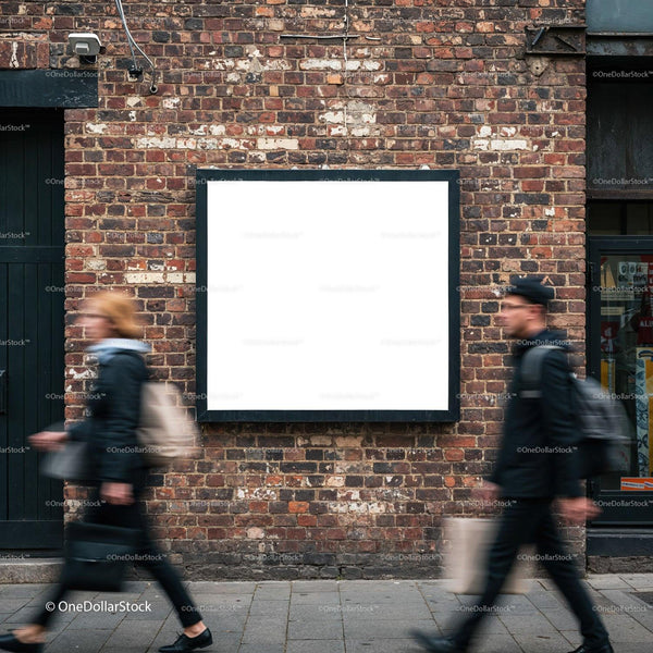 Two blurred pedestrians walking past blank billboard on brick wall JPG Mockup Image