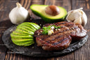 Grilled Steak with Sliced Avocado and Fresh Garlic on Rustic Wooden Board