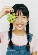 Happy Girl with Braided Hair Holding Green Grapes in Bright Indoor Scene
