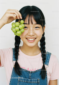 Happy Girl with Braided Hair Holding Green Grapes in Bright Indoor Scene