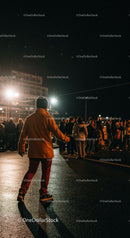 Man in orange jacket walking near nighttime crowd outdoors