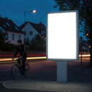 Illuminated blank billboard on city street at dusk