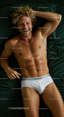 Smiling man relaxing on dark green bed in white briefs