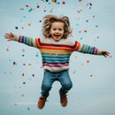 Joyful child jumping with confetti in colorful sweater