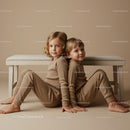 Two children sitting back to back in cozy outfits