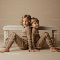Two children sitting back to back in cozy outfits