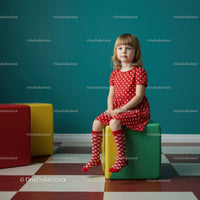 Little girl in red polka dot dress sitting on cube