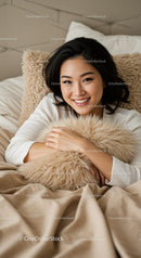 Smiling young woman relaxing with fluffy pillow in bed