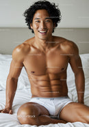 Fit young man smiling while sitting on bed in underwear