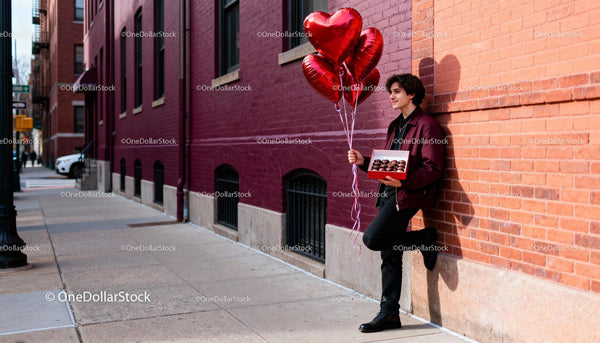 Young man holding heart balloons and chocolates outdoors