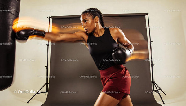 Focused female boxer training with punch bag in studio