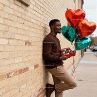 Man Holding Heart Balloons and Chocolates by Brick Wall