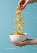 Hand pouring crunchy cornflakes into white bowl