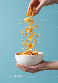 Hand pouring crunchy cornflakes into white bowl