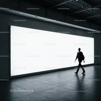 Silhouette of man walking past bright billboard in modern space