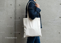 Person carrying blank white tote bag in urban setting