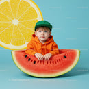 Toddler sitting inside giant watermelon slice on blue