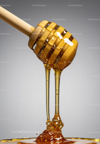 Golden honey dripping slowly from wooden dipper