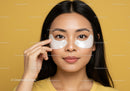 Woman Wearing Eye Patches Performing Skincare Routine Against Yellow Background