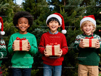 Happy children holding Christmas gifts by pine trees