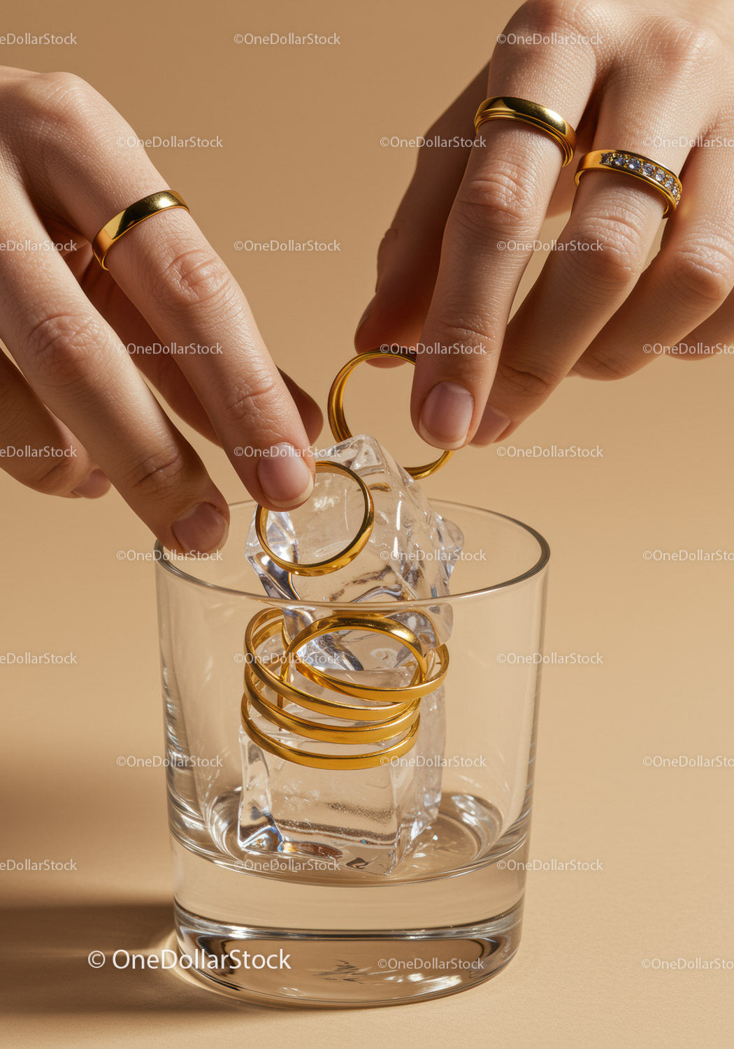 Hands placing gold rings on ice cubes in glass