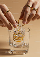 Hands placing gold rings on ice cubes in glass