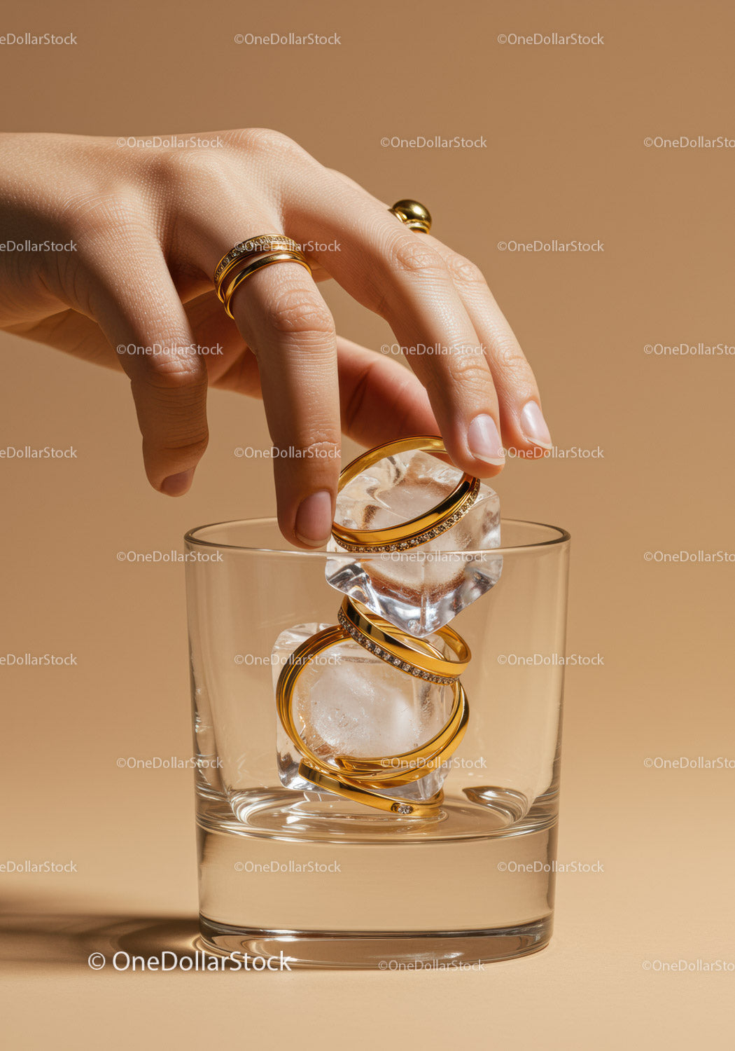 Hand Placing Gold Rings on Ice Cubes in Glass