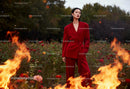 Confident woman in red suit standing among flowers and fire