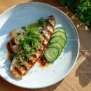 Grilled Fish with Cucumber Slices and Microgreens on a White Plate