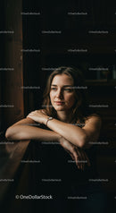 Thoughtful young woman resting arms on wooden window sill