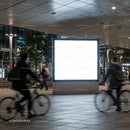 Urban night scene with illuminated blank billboard and cyclists