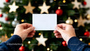 Hands holding blank card in front of Christmas tree JPG Mockup Image preview